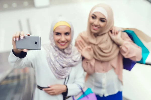 Arab women walking in shopping mall and taking selfie on smartphone