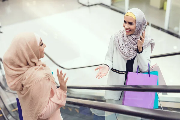 Arab women meeting in shopping mall, one woman taking on smartphone