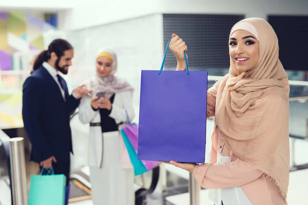 Arab woman holding shopping bag while her friends using smartphone