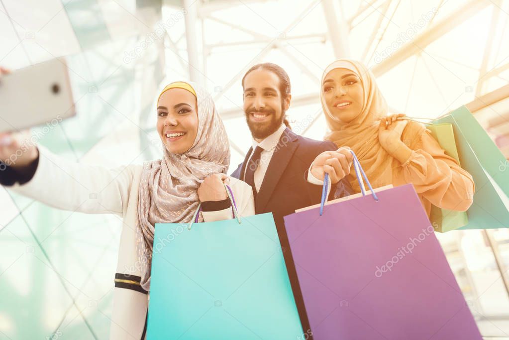 Arab women and man holding shopping bags and taking selfie 