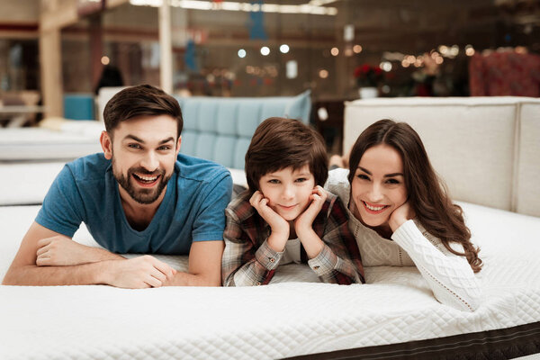 Parents and son relaxing on mattress in store and checking softness of mattress