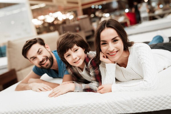 Parents and son relaxing on mattress in store and checking softness of mattress