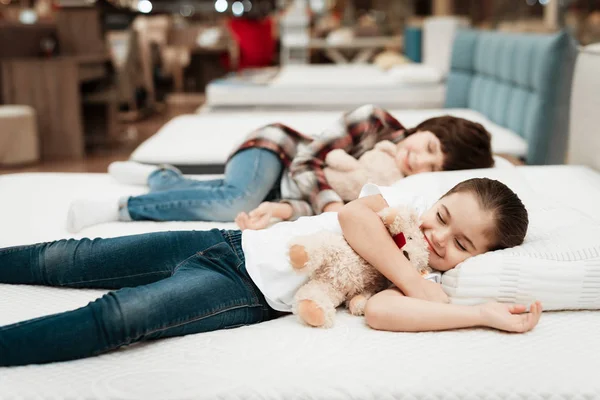 Девушка Обнимает Медведя Лежит Кровати Братом Магазине Матрасов — стоковое фото
