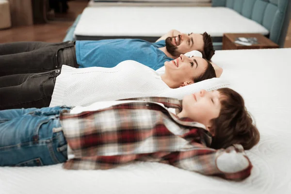Parents and son relaxing on mattress in store and checking softness of mattress