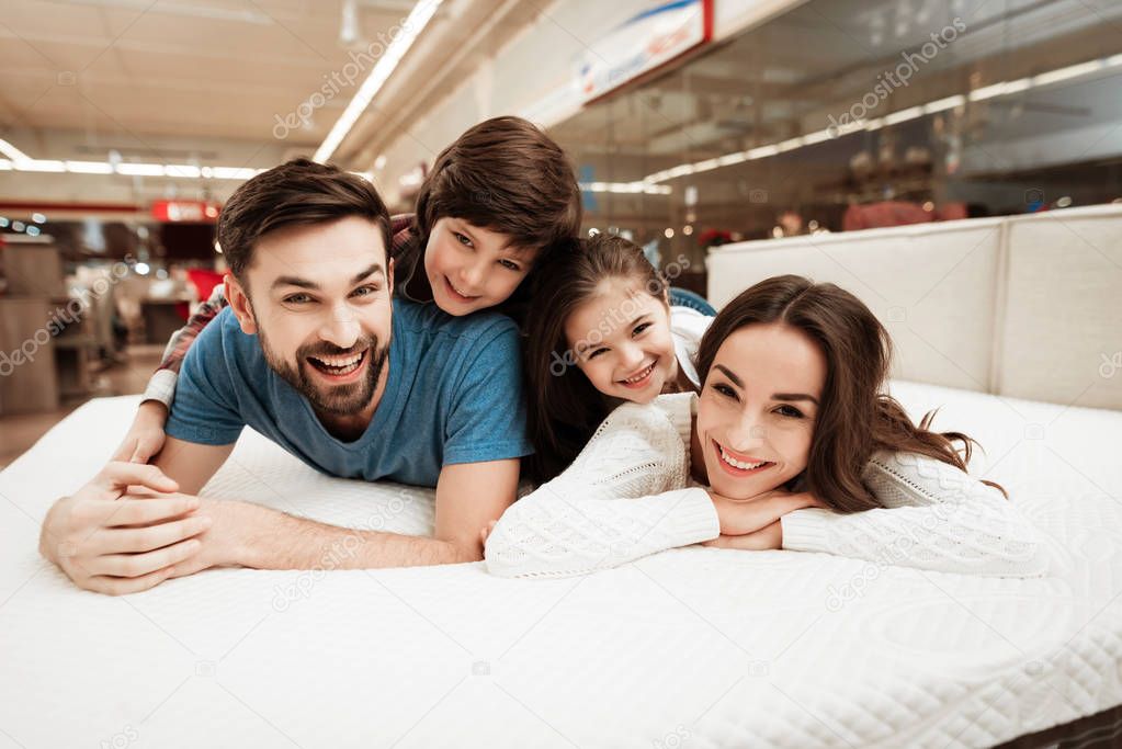 family checking softness of orthopedic mattress and lying on bed in furniture store