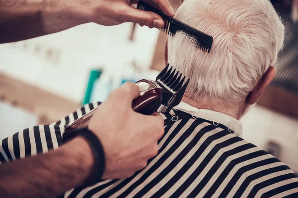 Hairdresser making haircut by hair trimmer in barbershop