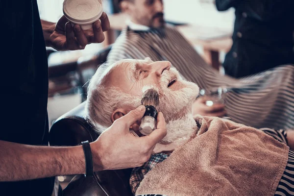 Barber bringing shaving cream on face by little brush