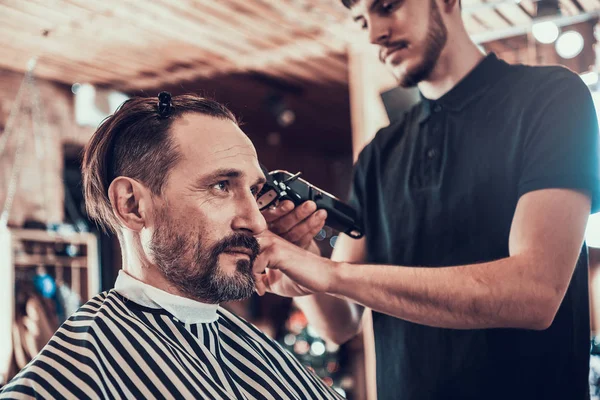 Hairdresser making haircut by hair trimmer in barbershop