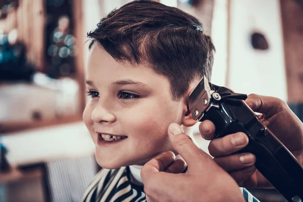 Hairdresser making haircut by hair trimmer in barbershop