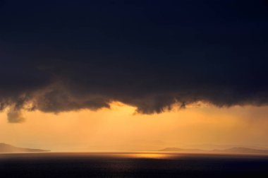 denizin üzerindeki kara bulutların arasından parlayan altın güneş