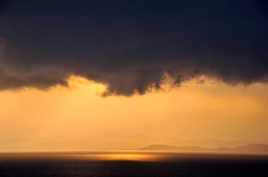 denizin üzerindeki kara bulutların arasından parlayan altın güneş