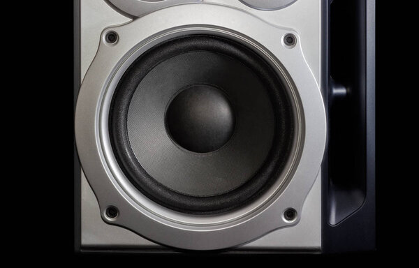 Fragment of a home loudspeaker in silvery housing with woofer closeup on the dark backgroun