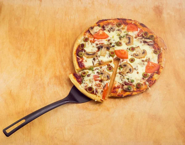 Partly sliced cooked pizza with spatula on wooden cutting board