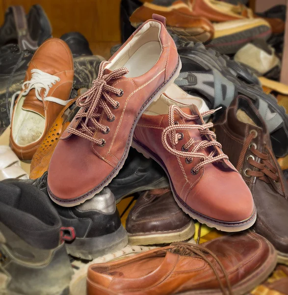 New mens shoes on pile of old different worn footwear — Stock Photo, Image