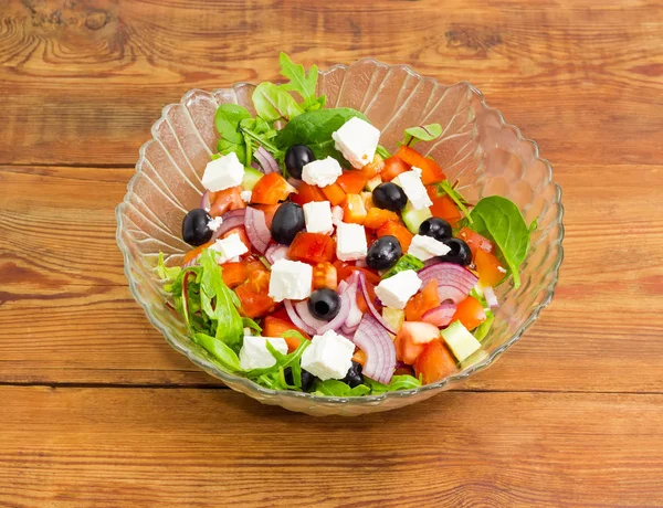 Greek salad in glass salad bowl on old wooden surface