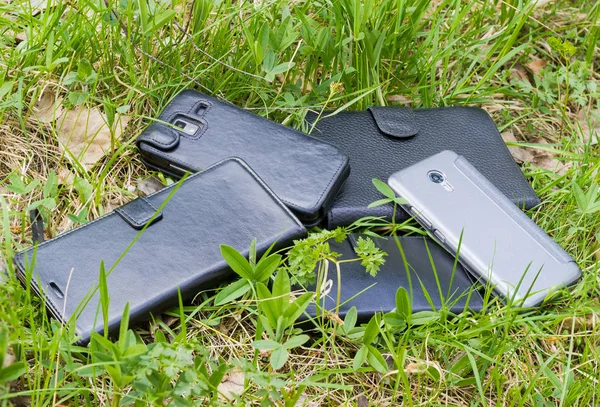 Varios teléfonos inteligentes en diferentes cubiertas entre la hierba — Foto de Stock