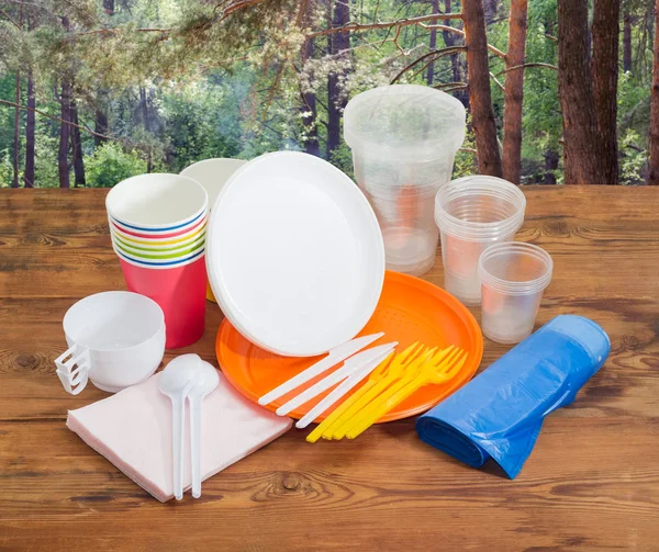 Different disposable cutlery on wooden planks against pine forest — Stock Photo, Image