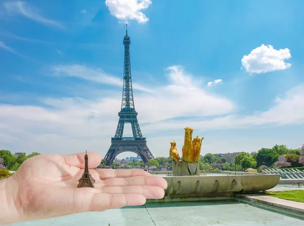 Eiffel Tower model on man\'s palm against Eiffel Tower