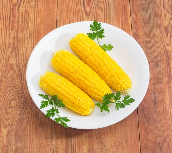Вареная сладкая кукуруза на белом блюде на деревянной поверхности — стоковое фото