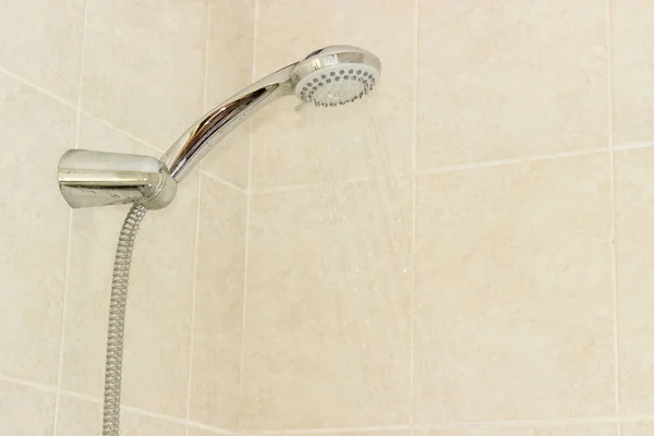 Shower head in holder on wall with beige tiles