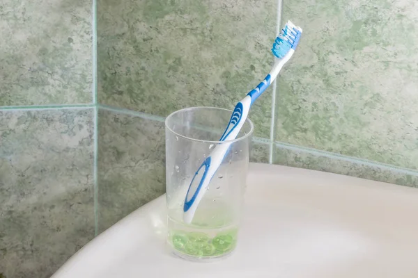 Toothbrush in glass for toothbrushes against of green tile — Stock Photo, Image