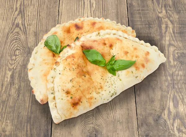 Zwei gekochte Calzone mit Basilikumzweigen auf rustikaler Holzoberfläche — Stockfoto