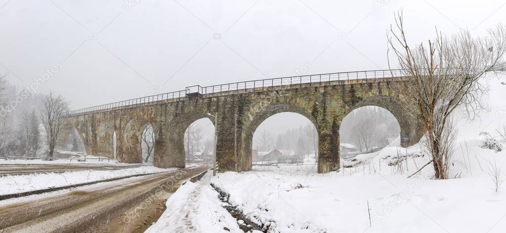 Old stone railway viaduct in Carpathian Mountains during snowfall