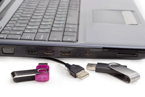Два USB флэш-накопителя и USB-кабель против ноутбука — стоковое фото