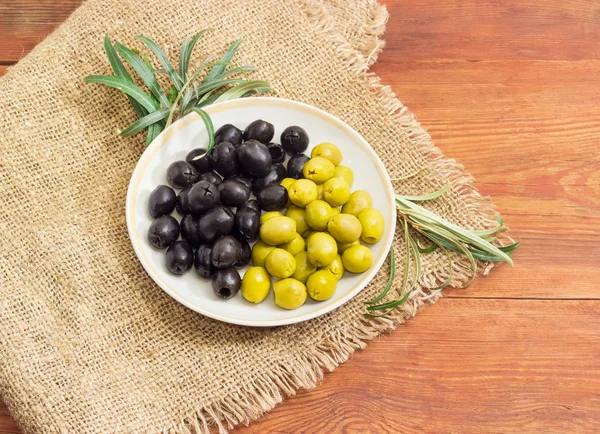 Black and green olives and olive branches on wooden surface