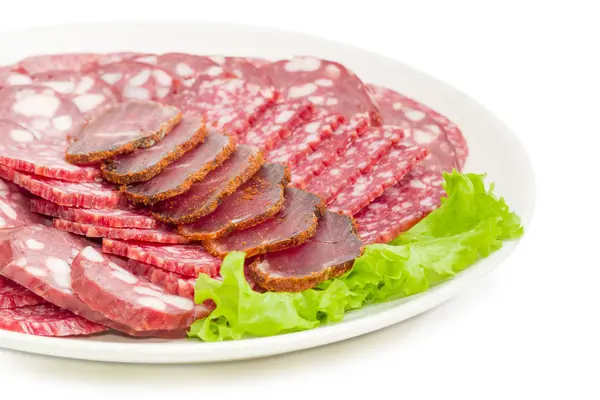 Trancher différents produits de viande sur la laitue sur un plat blanc gros plan — Photo