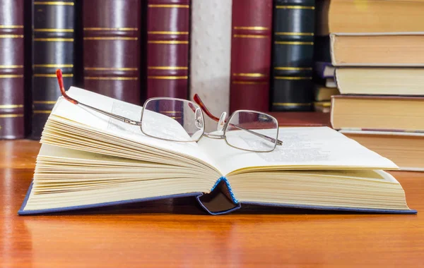 Eyeglasses on the open book against of the other books — Stock Photo, Image