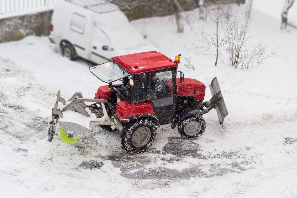 Small red tractor snow plow in courtyard during snowfall