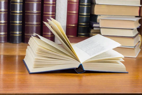 Open book on wooden surface against background of other books — Stock Photo, Image
