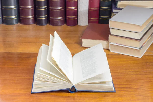 Open book on wooden table against background of other books — Stock Photo, Image