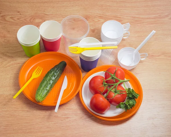 Different disposable cutlery and vegetables on a wooden table