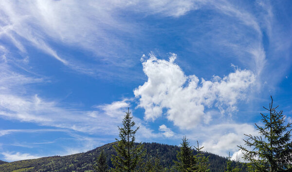 Небо с перистыми и кучевыми облаками над горным склоном
