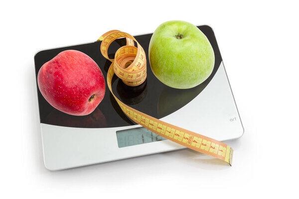 Apples and tapeline on kitchen scales, concept of excess weight