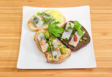 Salamura ringa balığı filetosu çanak üzerinde üç farklı açık sandviçle