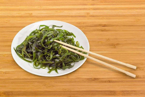 Insalata di alghe marinate su piatto bianco con bacchette di bambù — Foto Stock