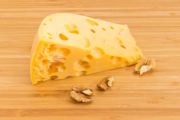 Pedazo de queso suizo y nueces en la tabla de cortar de bambú —  Fotos de Stock