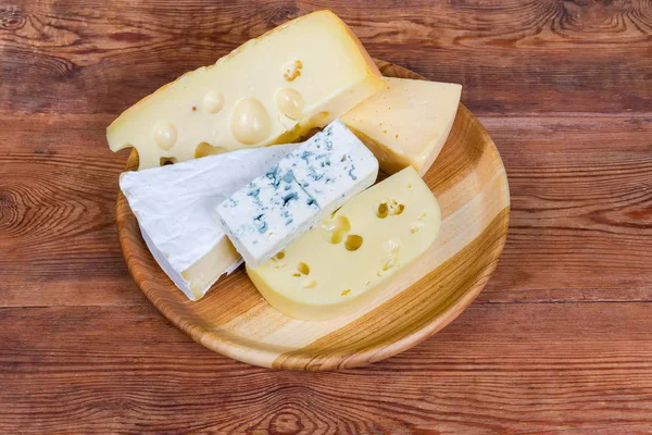 Morceaux de fromage différent sur un plat en bois sur une table rustique — Photo