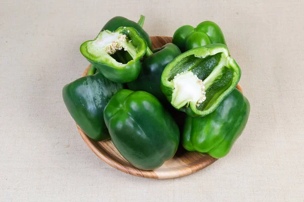 Fresh green bell peppers on wooden dish on cloth surface