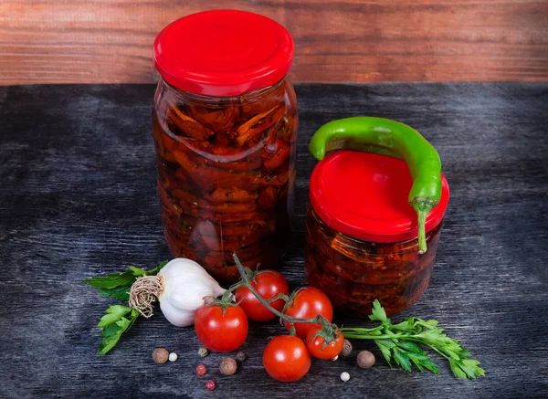 Tomates secos en aceite de oliva en frascos de vidrio entre ingredientes —  Fotos de Stock