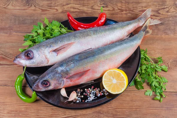 Carcasas de pescado Redbait sin cocer y especias en plato negro —  Fotos de Stock