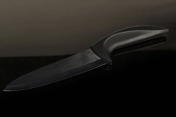 Kitchen ceramic knife with black blade on dark reflective surface