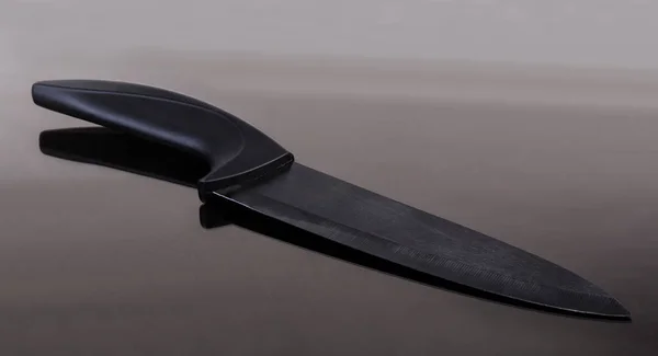 Faca de cerâmica de cozinha com lâmina preta na superfície reflexiva escura — Fotografia de Stock