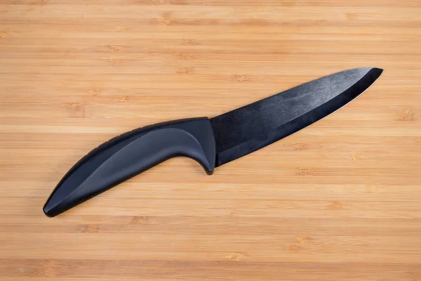 Black kitchen knife with ceramic blade on wooden cutting board