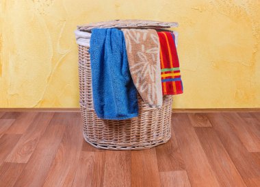 Ahşap hasır çamaşır sepeti yerde ve banyo havluları.