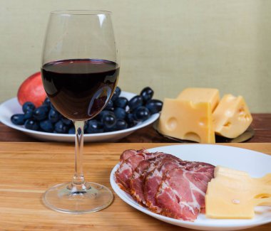 Peynir karşısında kırmızı şarap, pişmiş domuz eti, meyveler yakın plan.