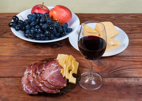 Vino tinto contra queso, cerdo curado, frutas en mesa rústica —  Fotos de Stock